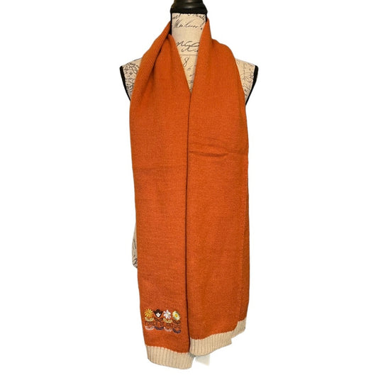An orange knit scarf with cream ribbed trim and small embroidered flowers near one end, displayed on a dress form against a white background.