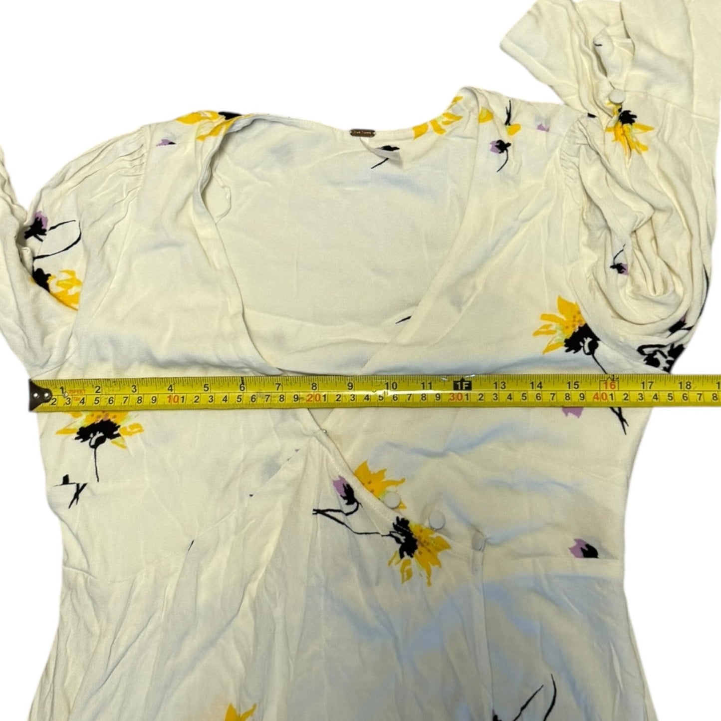 A dress with a yellow and black sunflower print, shown with a yellow tape measure across the chest to indicate size.