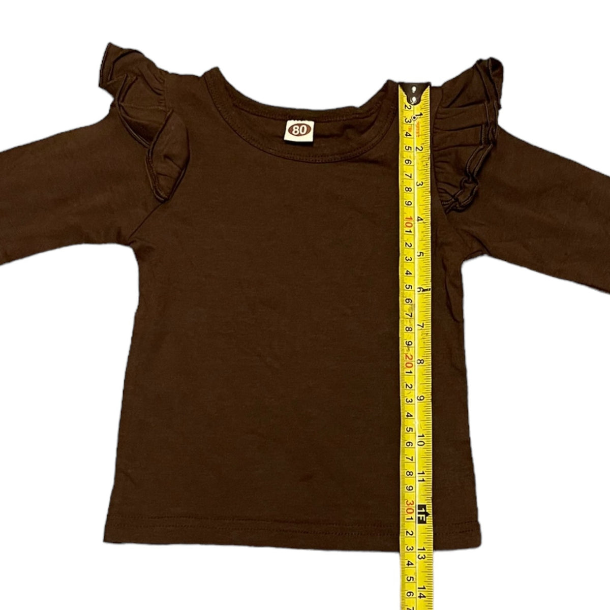 A dark brown long-sleeve top with ruffled shoulder details, shown flat on a white background with a yellow measuring tape running vertically to indicate size.