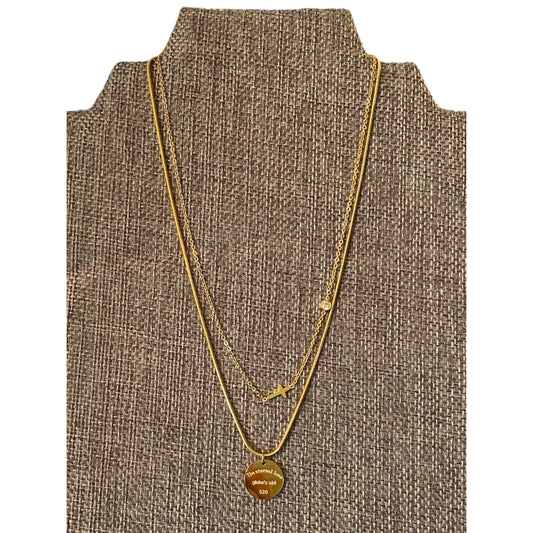 A gold layered necklace with a circular engraved pendant displayed on a brown woven jewelry bust against a white background.