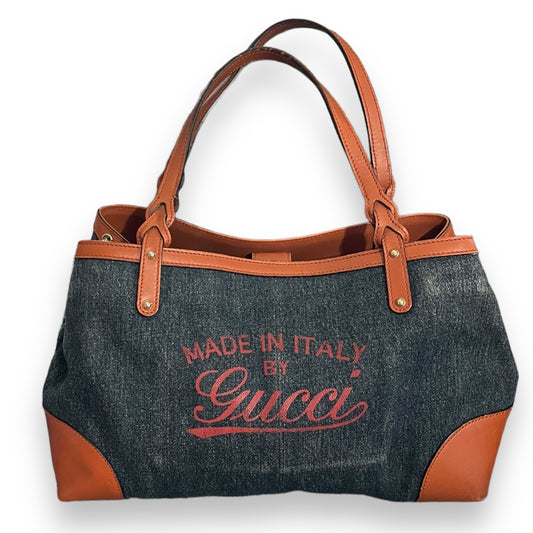 Denim handbag with brown leather accents and 'Made in Italy by Gucci' text on a white background