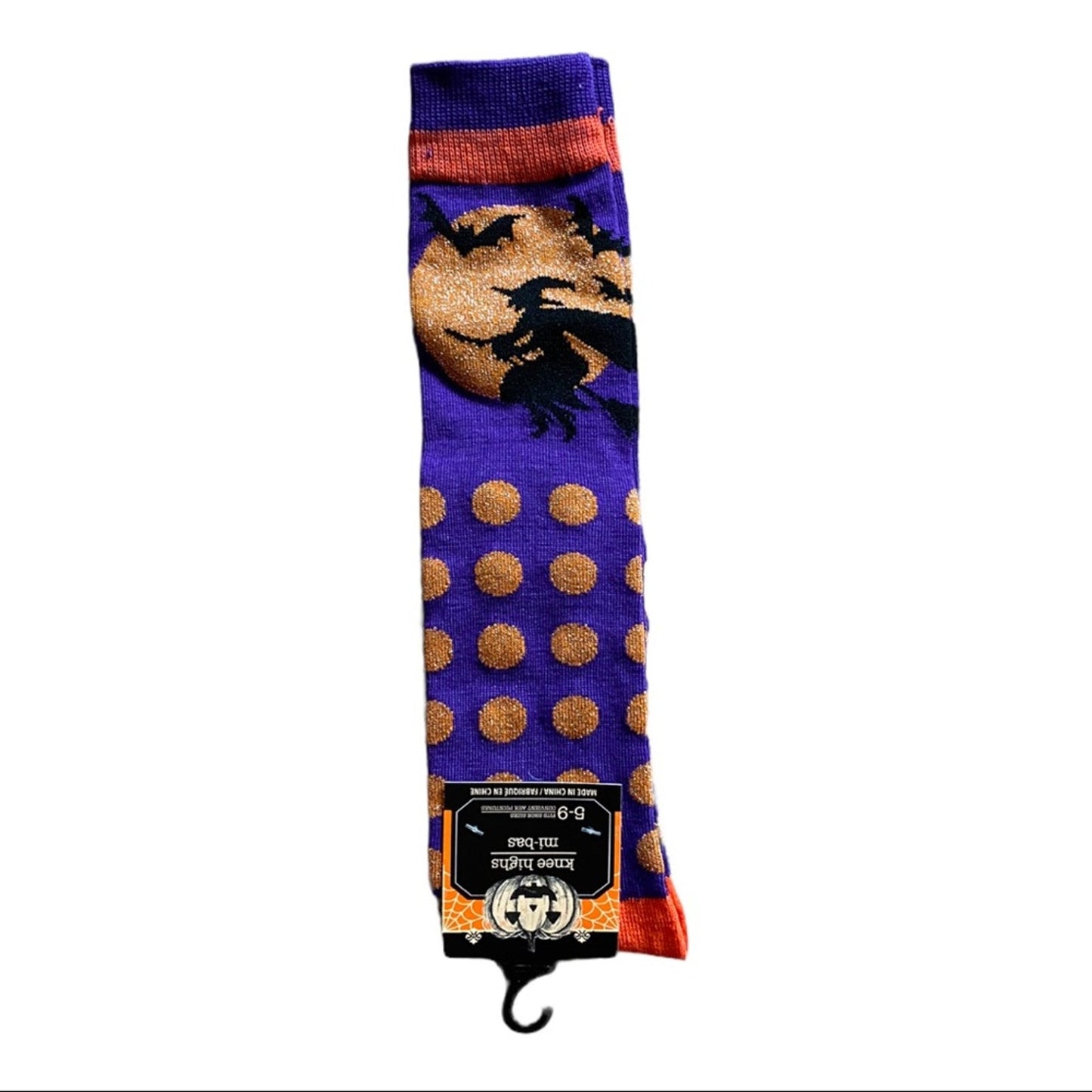 A purple Halloween crew socks with a gold moon and witch graphic, gold polka dots, and orange cuff/heel details, shown on a white background with its retail hanger tag attached.