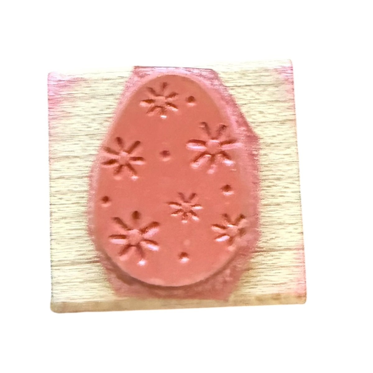 A pink rubber stamp with an Easter egg design featuring flowers and dot patterns, mounted on a light-colored wooden block.