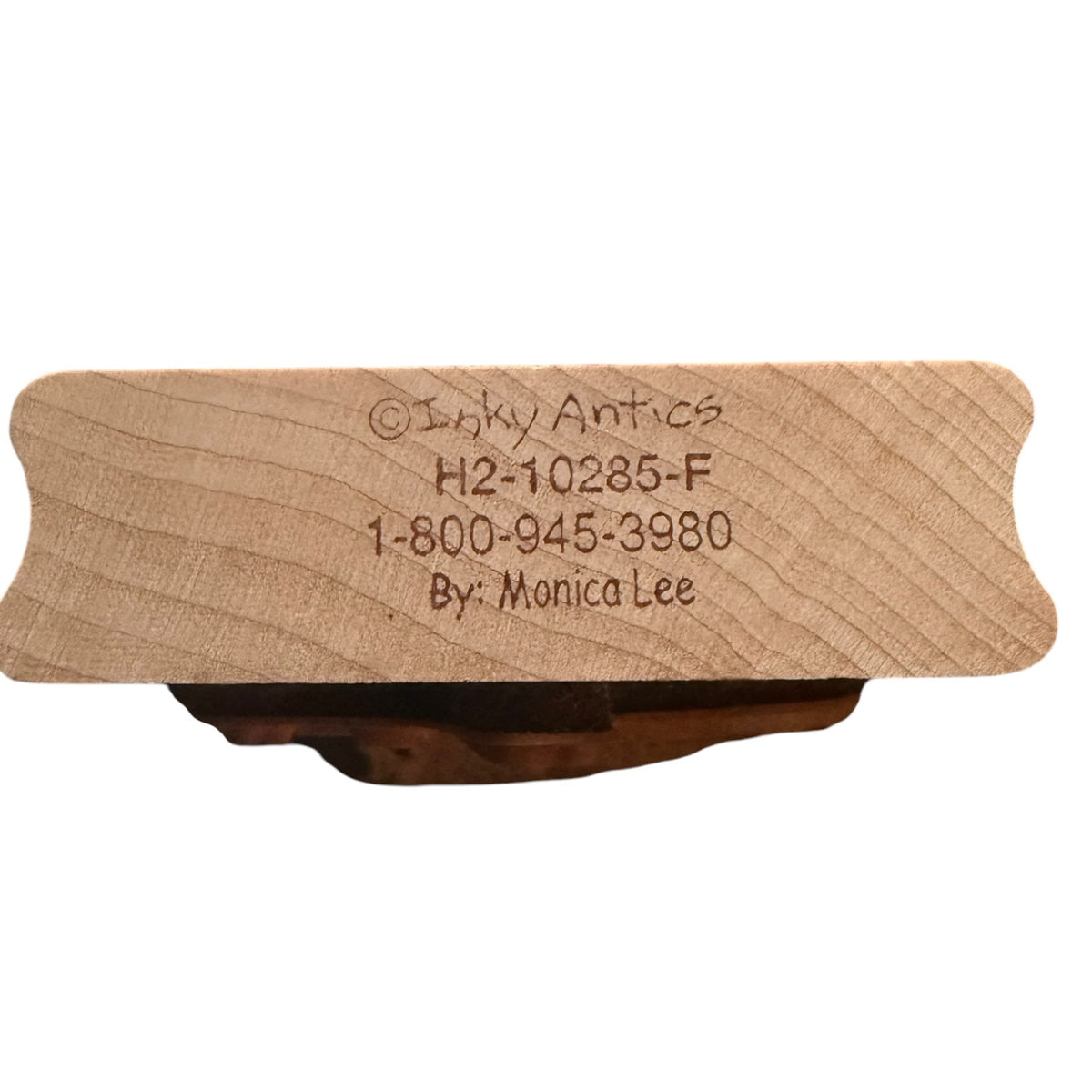 A close-up of a natural wood stamp block with the text '©Inky Antics H2-10285-F 1-800-945-3980 By: Monica Lee' on a plain white background.