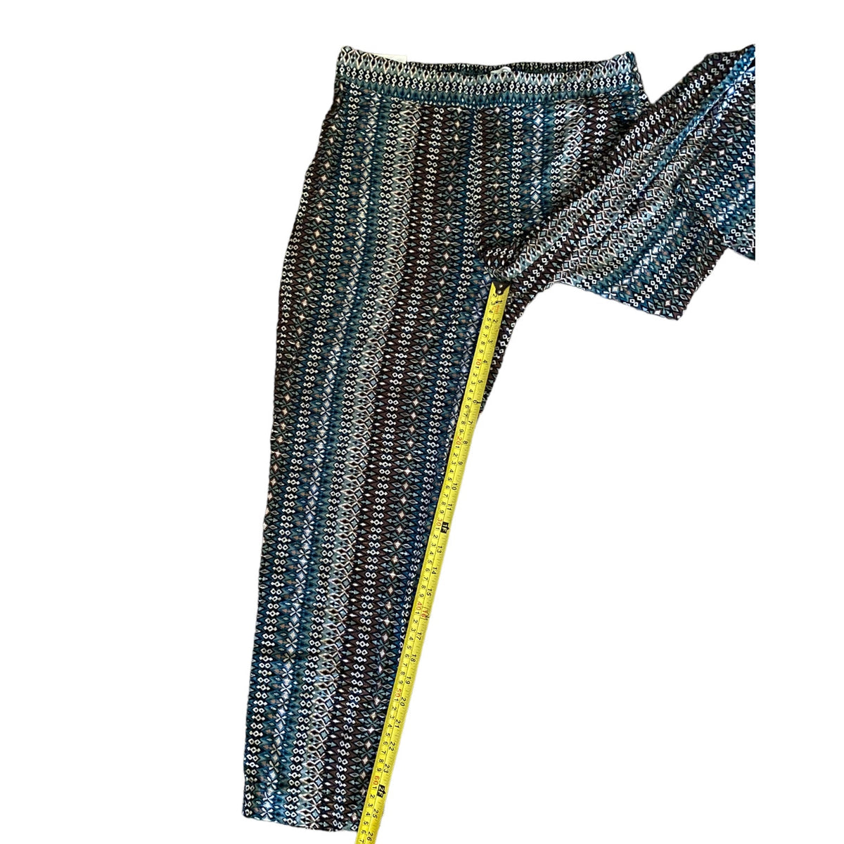 A pair of pants, striped pattern in multicolor, shown with a yellow measuring tape running down the leg to indicate size.
