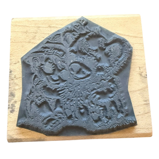 A dark gray carved rubber stamp , mounted on a square light wood block against a white background.