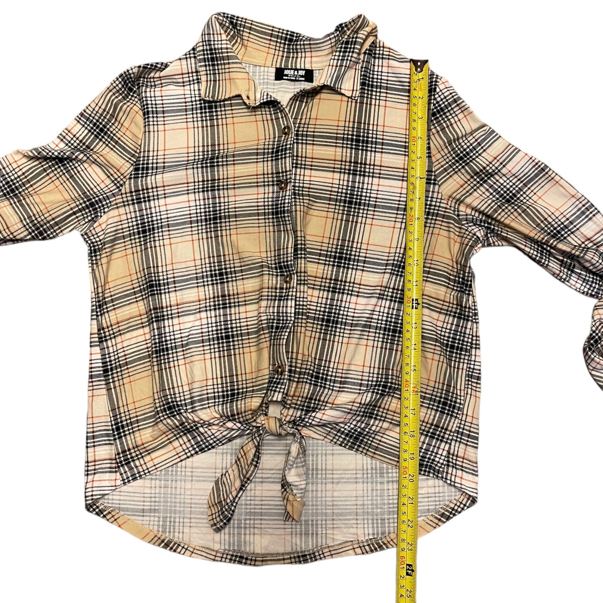 A beige plaid button-up shirt with a front knot detail, displayed flat with a yellow measuring tape running vertically along the side to show the length.