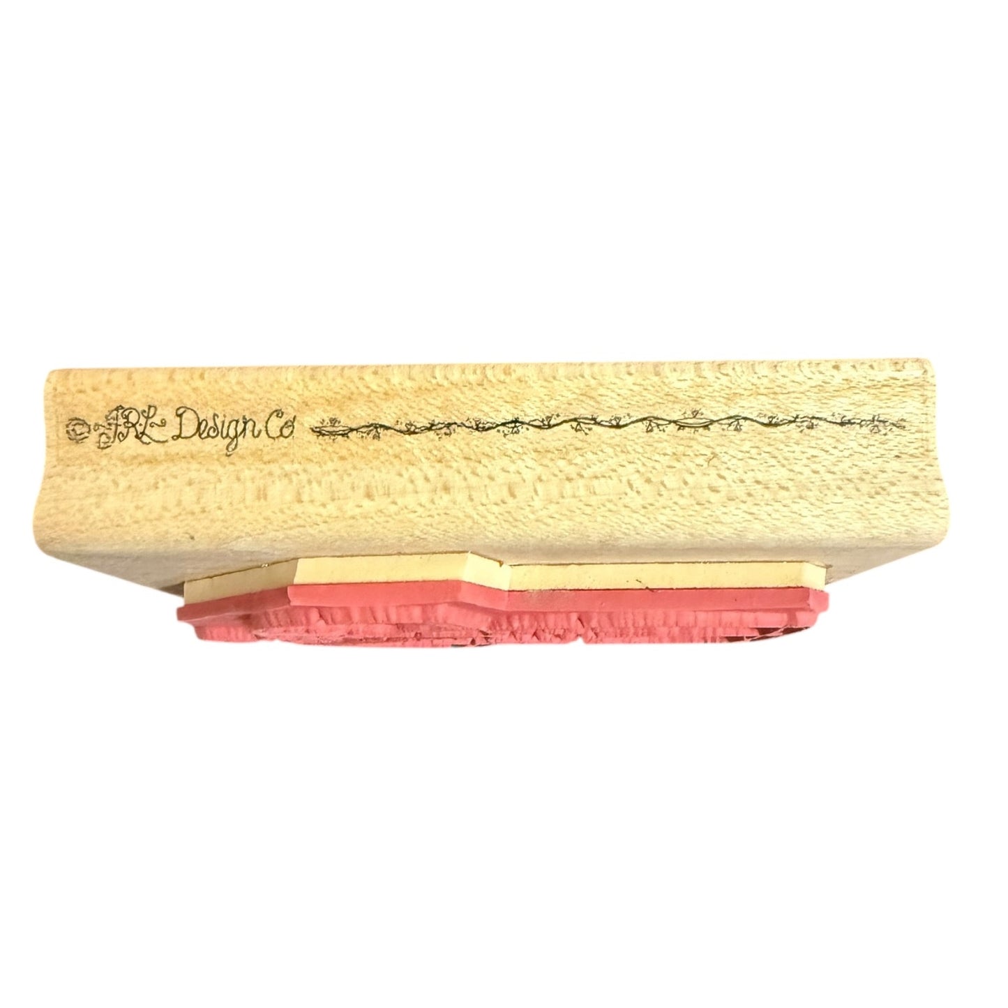A close-up of a stamp block with a textured beige wooden top featuring the brand name 'JRL Design Co' in black script, supported by layered pink and beige rubber stamps, shown against a plain white background.