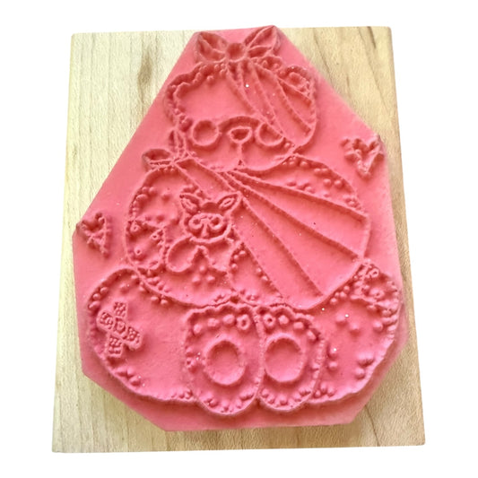 A pink rubber stamp with a teddy bear design, displayed on a light wood block against a white background.