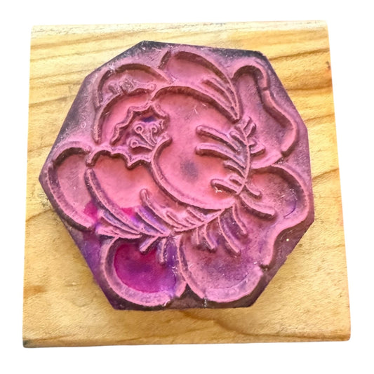 A wooden stamp block with a carved floral design, shown on a light wood background.