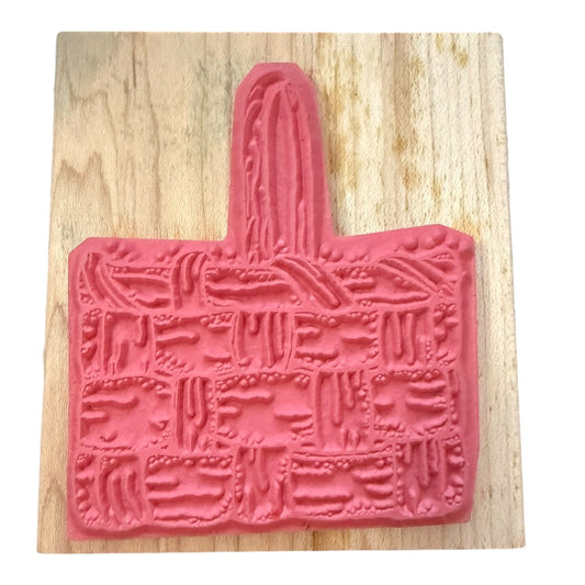 A pink rubber stamp shaped like a woven basket with a handle, shown on a light wood against a white background.