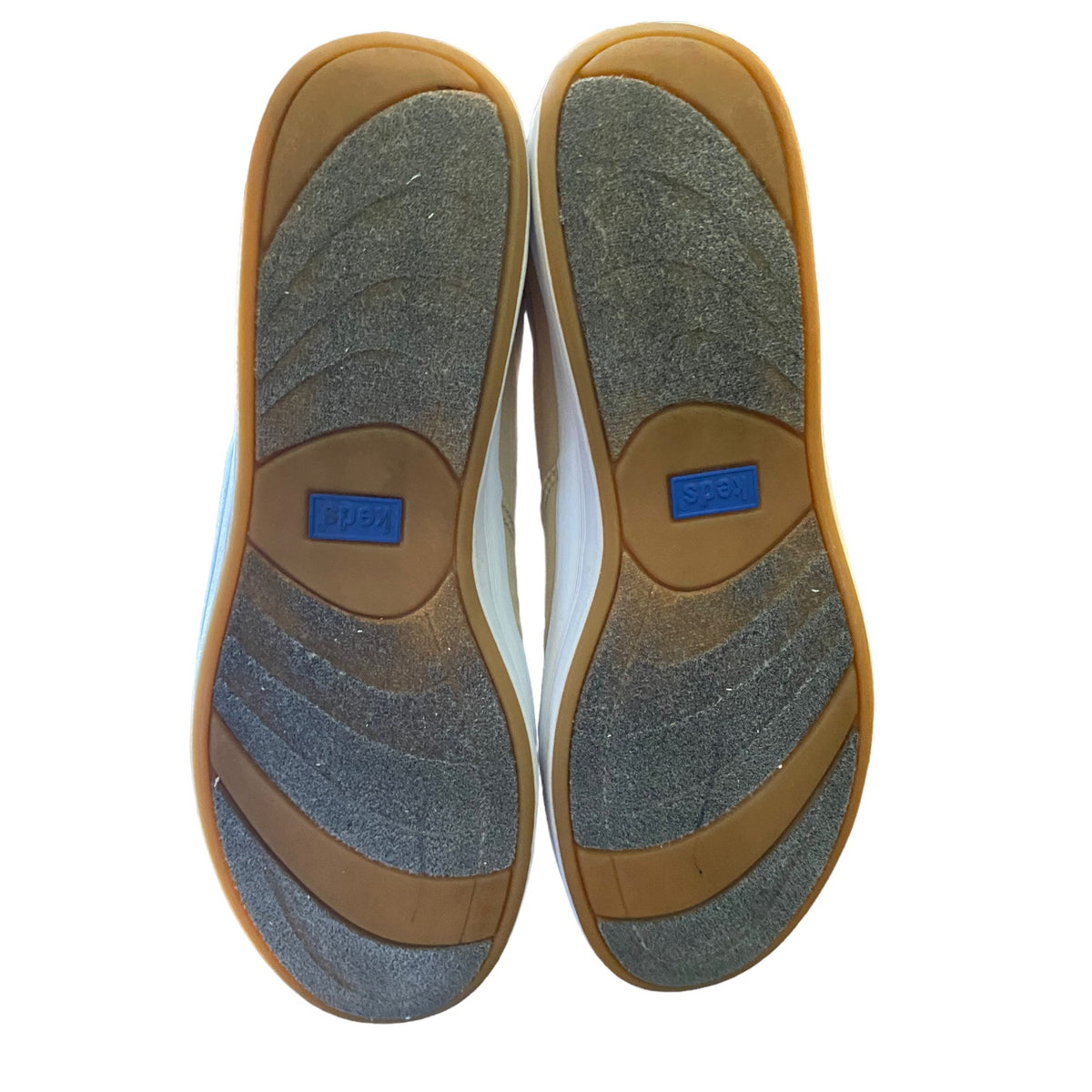 Top-down view of a pair of shoes showing the outsoles, featuring a textured gray and brown tread pattern with a blue brand patch in the center of each sole.