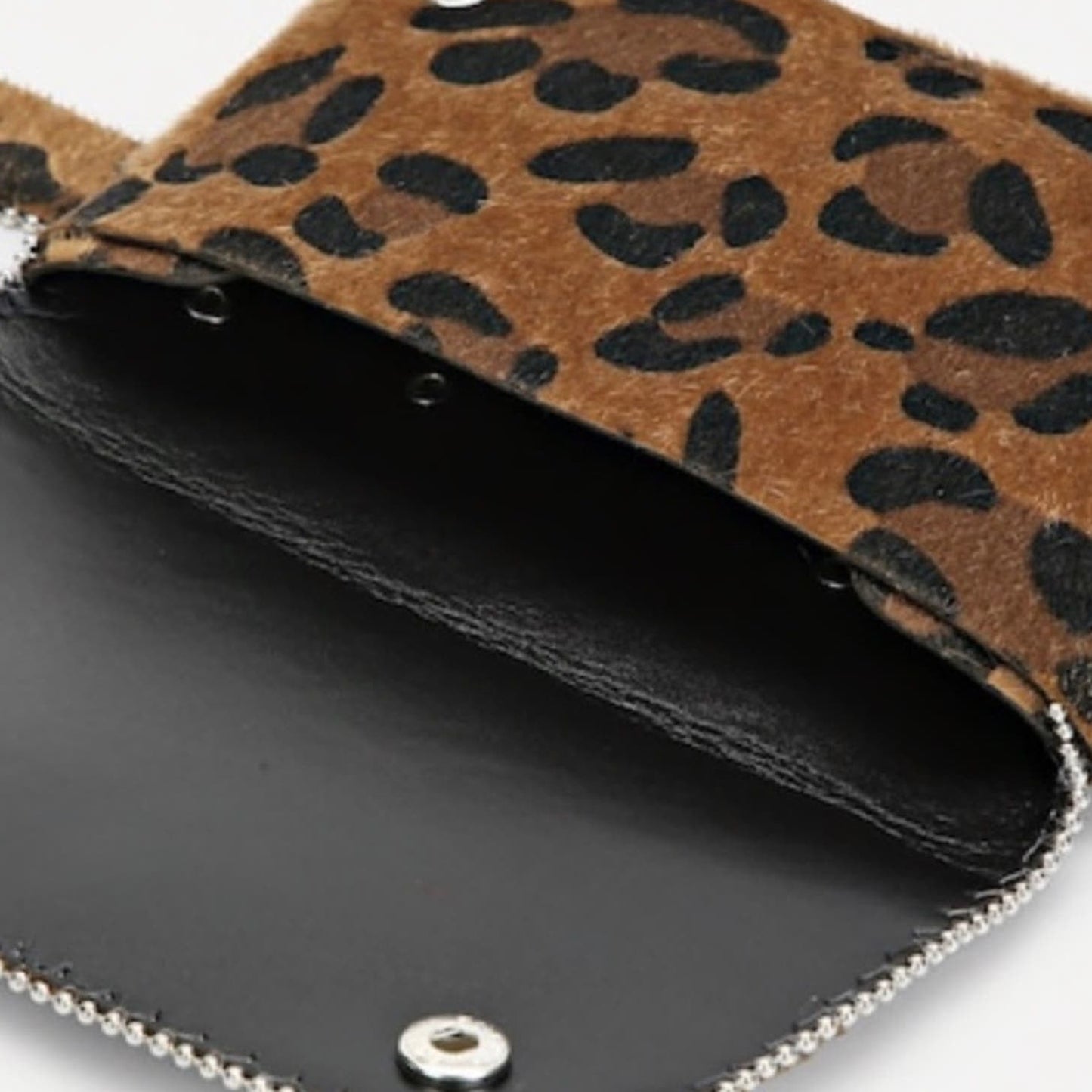 Close-up of a leopard print pouch with a brown and black animal pattern, shown open to reveal a black interior and silver-tone trim.