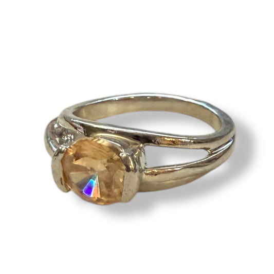 A silver-toned ring featuring a large, round, faceted orange crystal gemstone in a prong setting, shown on a white background with a soft shadow.