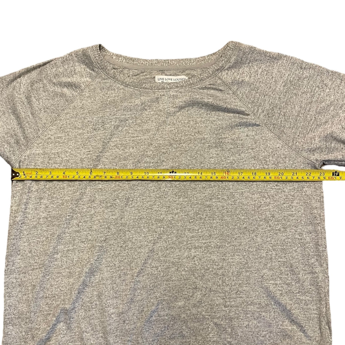 A heather gray shirt laid flat on a white background, with a yellow tape measure stretched horizontally across the chest to show the width.