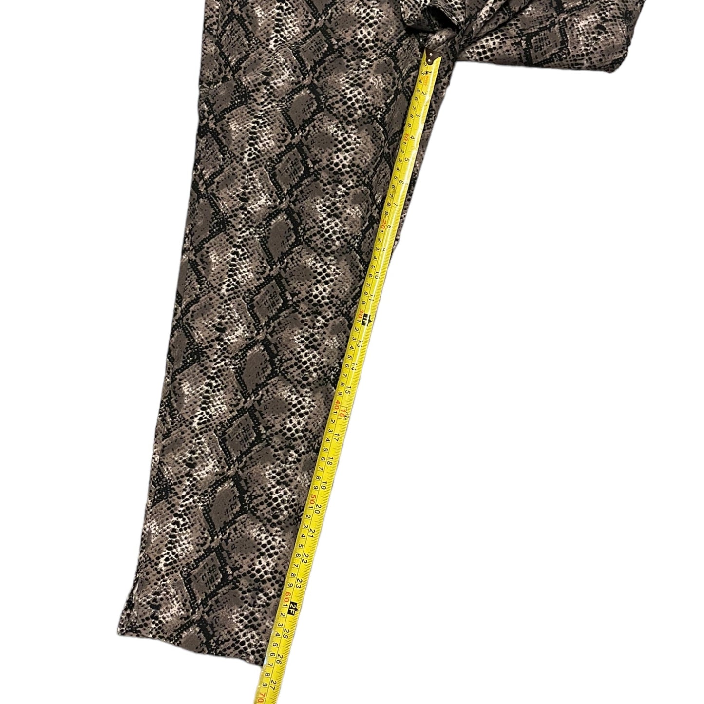 A close-up of a snakeskin-patterned capri pants with a yellow measuring tape running vertically along one edge, shown on a plain white background.
