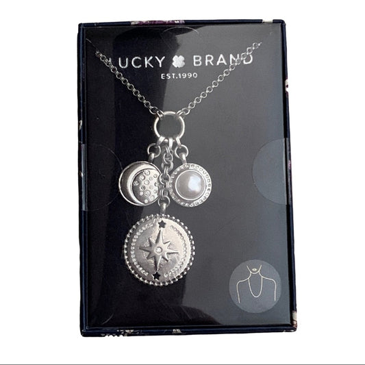 Silver-toned charm necklace with three charms on a silver chain, presented in its original Lucky Brand retail box.