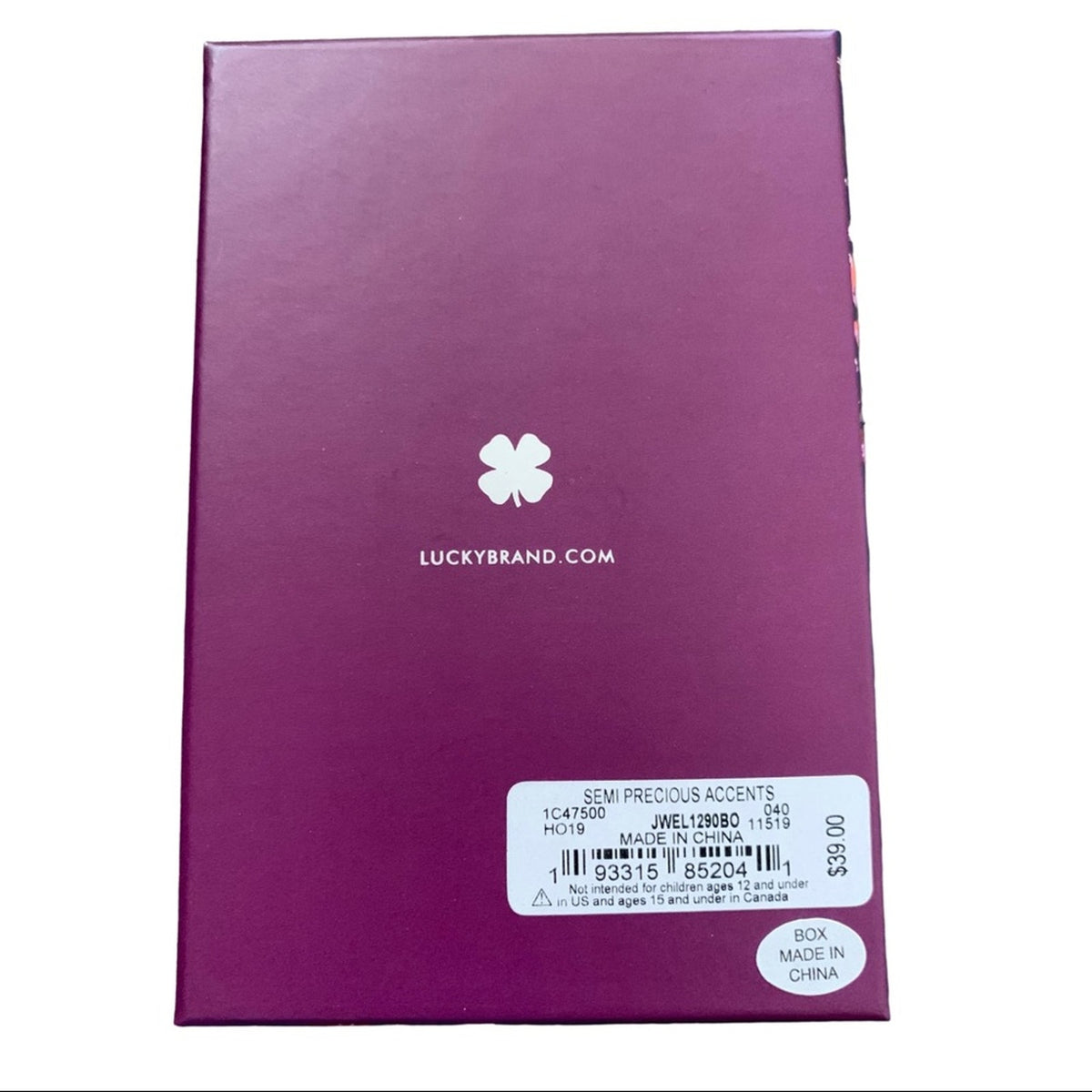 A purple rectangular product box for Lucky Brand, featuring a white four-leaf clover logo and 'LUCYBRAND.COM' printed on the front, with a white product info label at the bottom.