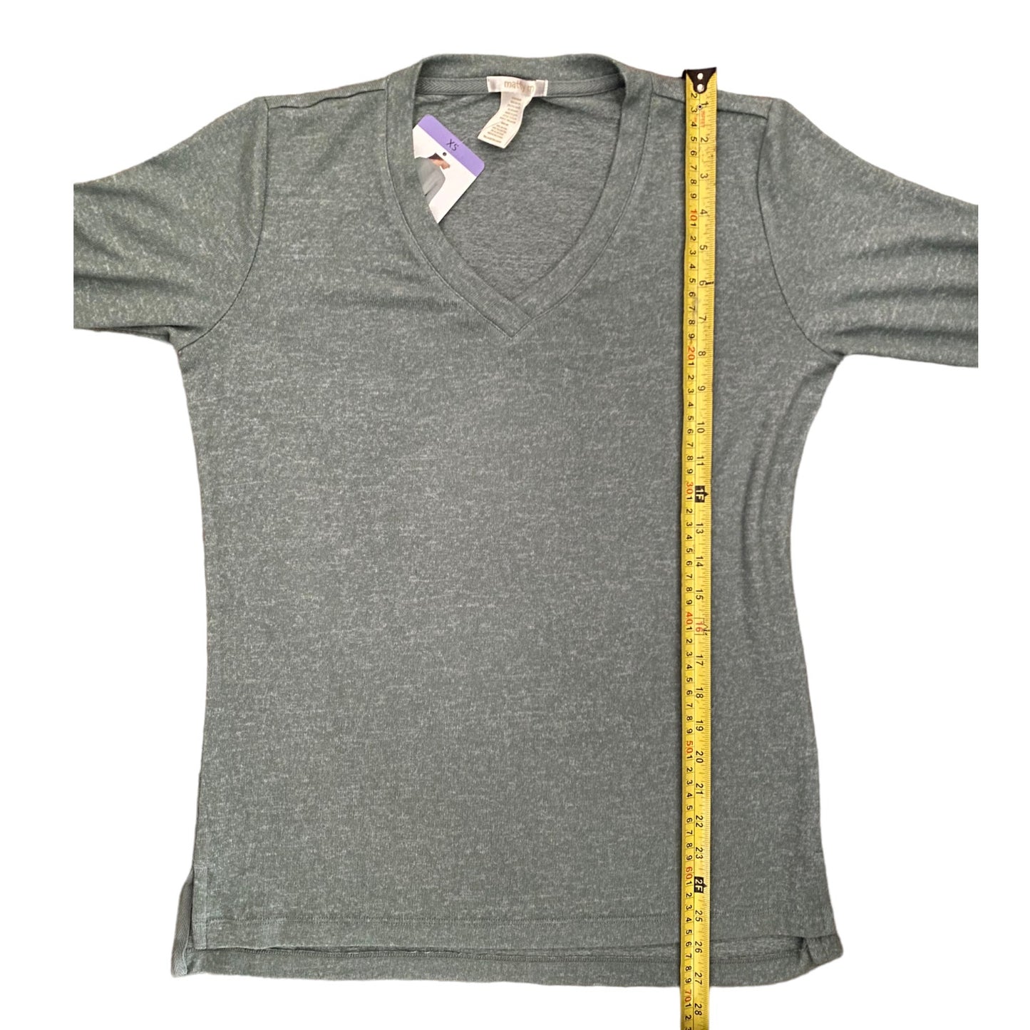 A green V-neck shirt laid flat on a white background, with a yellow measuring tape standing vertically along the right side to show the garment's height.