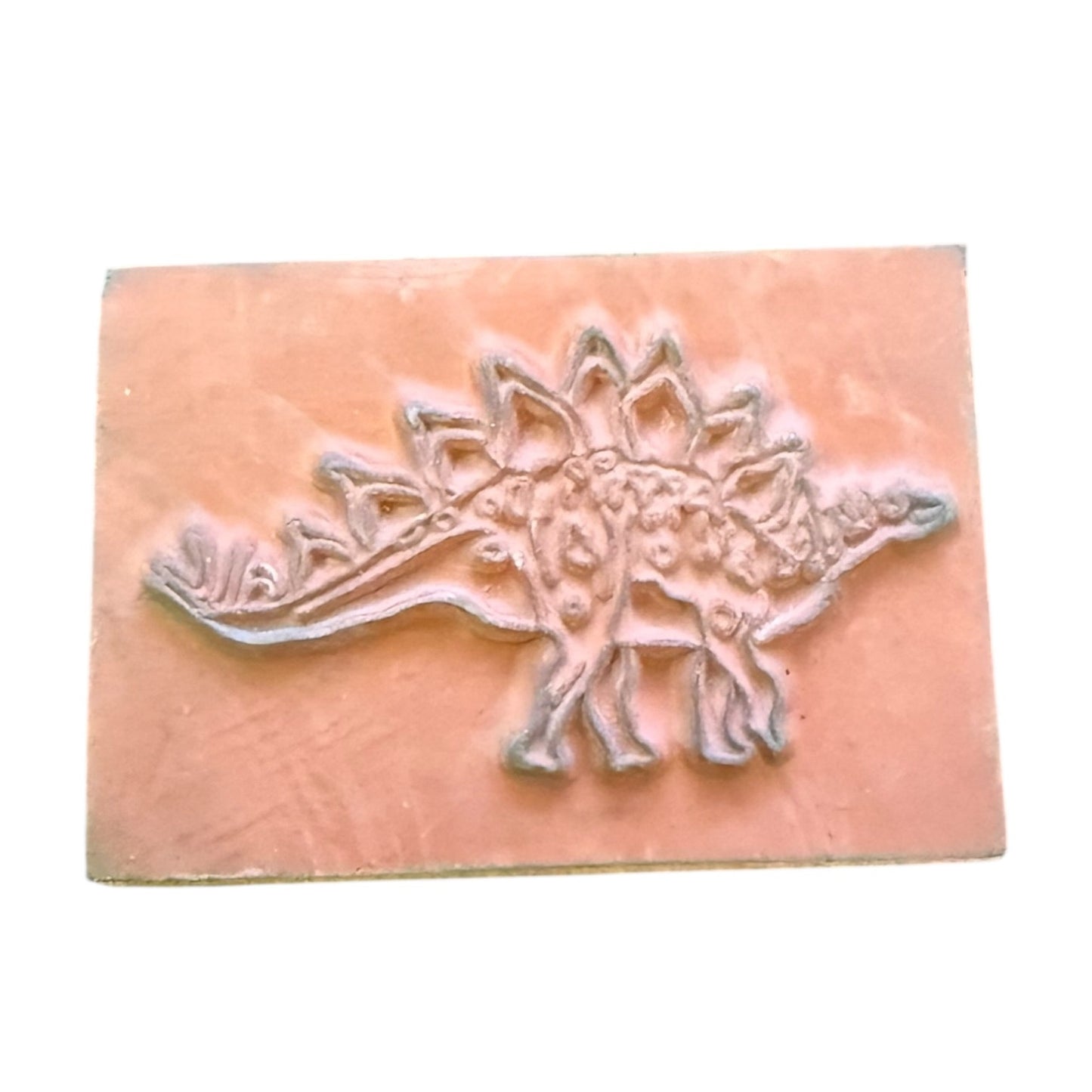 A rectangular stamp featuring an embossed dinosaur design, shown against a plain white background.