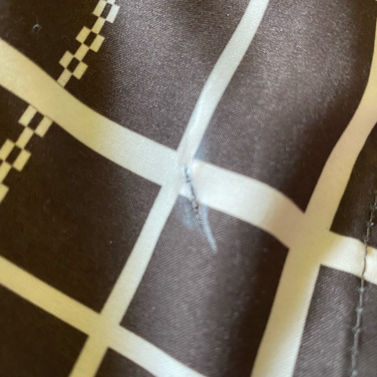 Close-up of a dark brown fabric with a cream-colored grid pattern and a visible white scratch or abrasion on the surface.