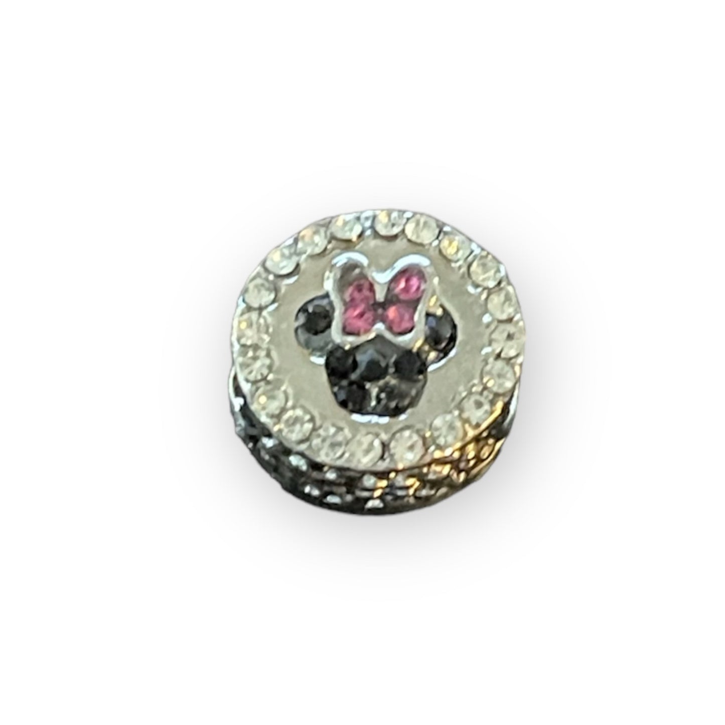 A round silver charm featuring a Minnie Mouse silhouette with pink bow details, surrounded by clear rhinestones on a white background.