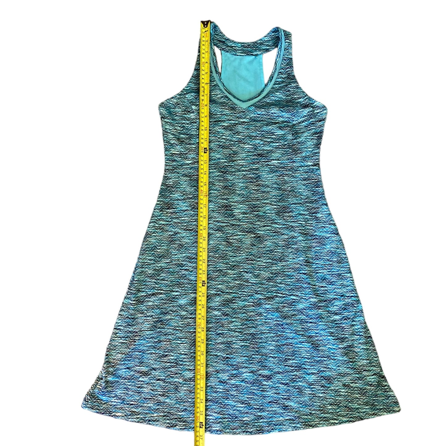 A sleeveless racerback dress in a blue , shown flat against a white background with a yellow measuring tape running vertically down the center.
