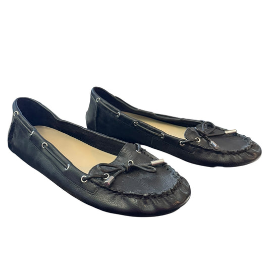 A pair of black leather moccasin-style flats with silver metal tassel details and silver eyelets, shown on a plain white background.