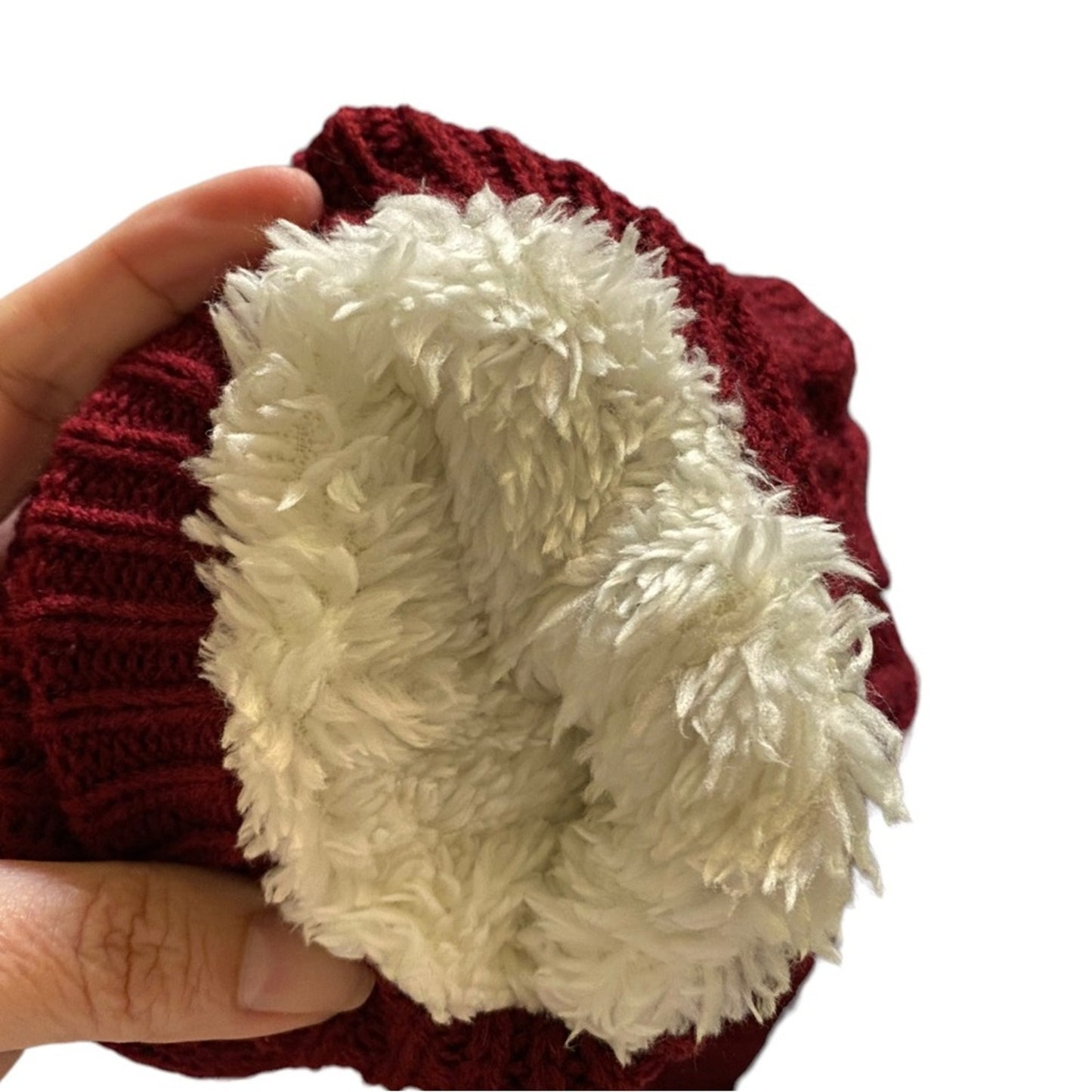 A close-up of a dark red ribbed knit socks with a thick, fluffy cream sherpa lining, held by a hand against a white background.