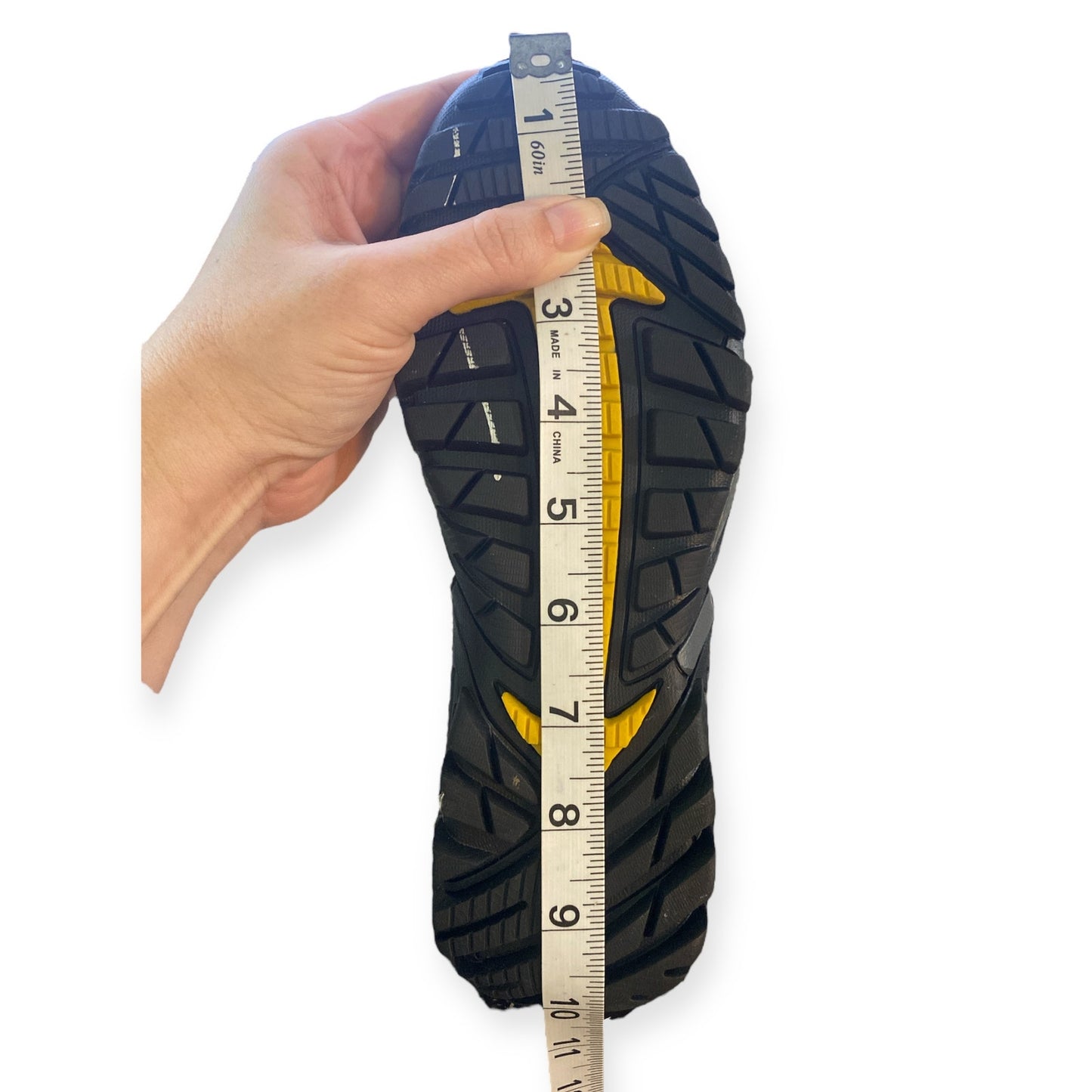 Hand holding a shoe with a measuring tape to show tread depth on a white background