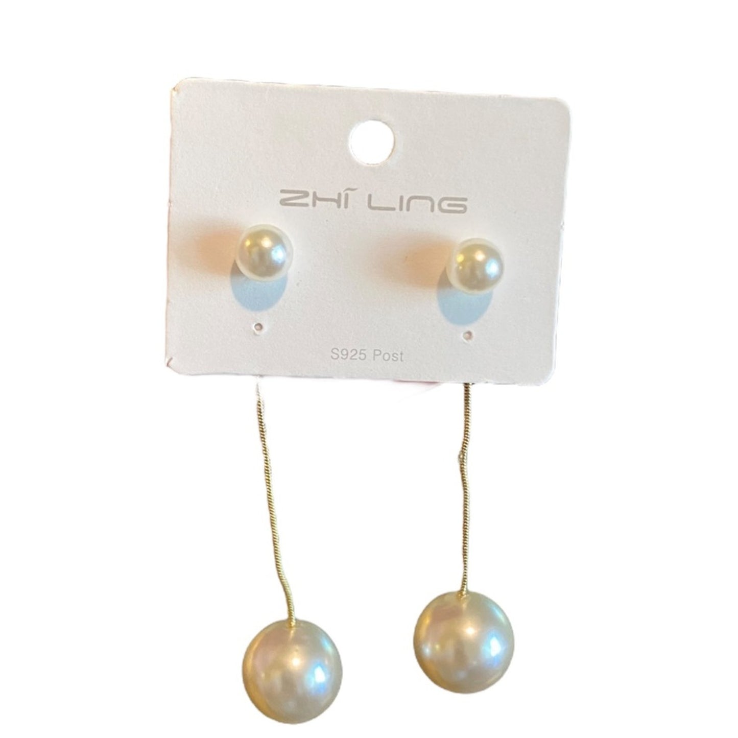 Gold tone pearl drop earrings on a white card on a white background