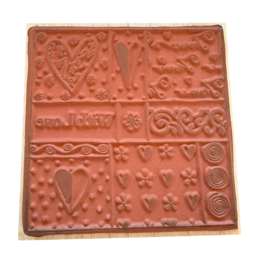 A square terracotta-colored rubber stamp with embossed floral, heart, and scroll designs, mounted on a light-colored wooden block against a white background.