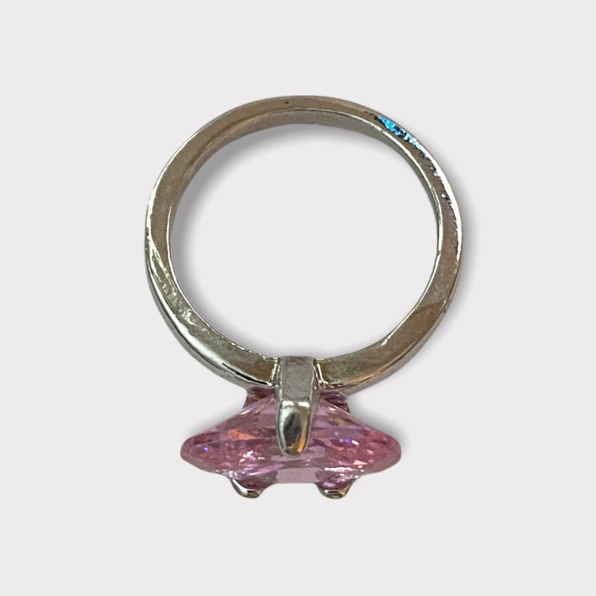 A silver ring featuring oval shaped pink stone from a top view, photographed against a light gray background.