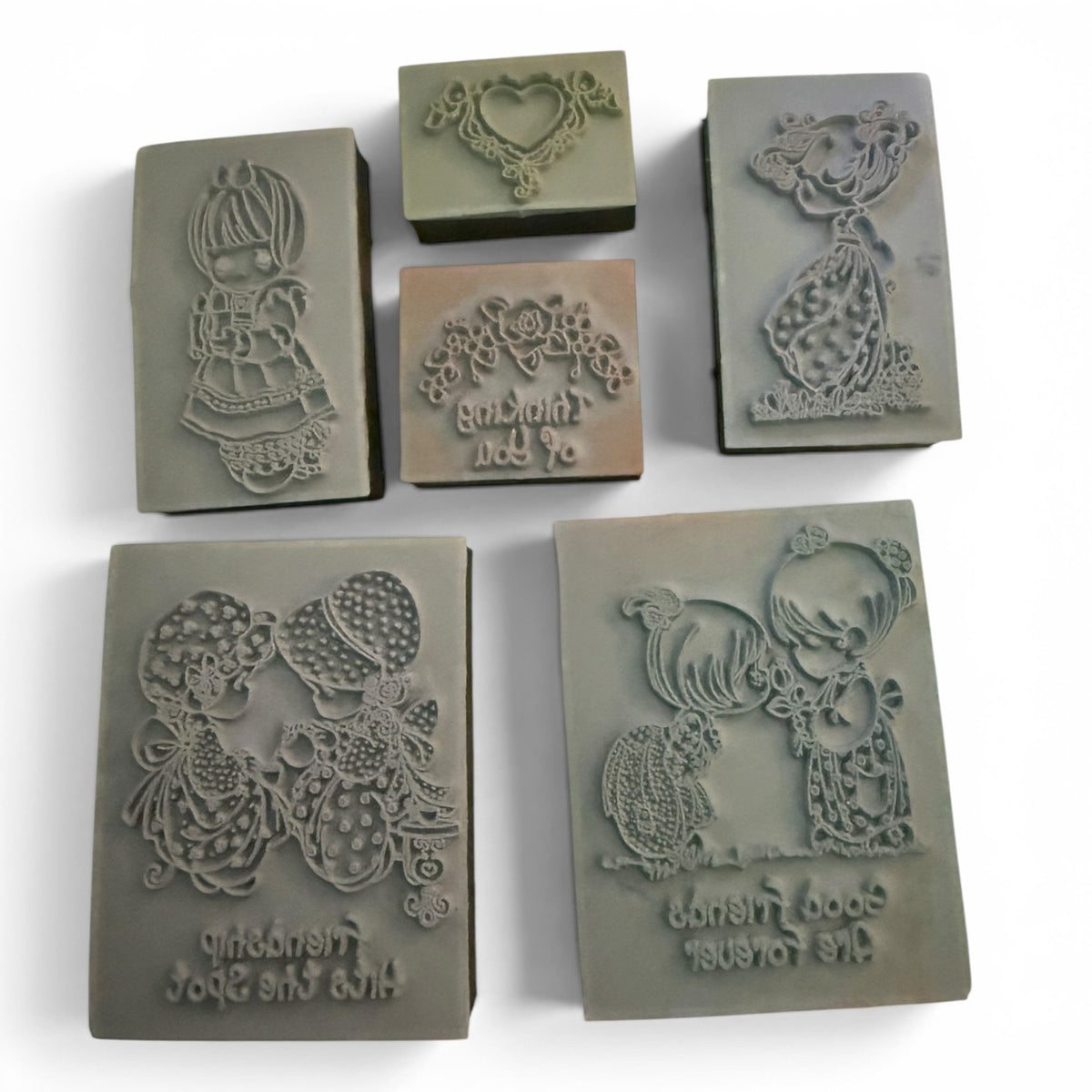 Six rectangular gray rubber stamp arranged on a white background, each featuring different embossed designs including a girl, a heart motif, flowers, and figures with script text.