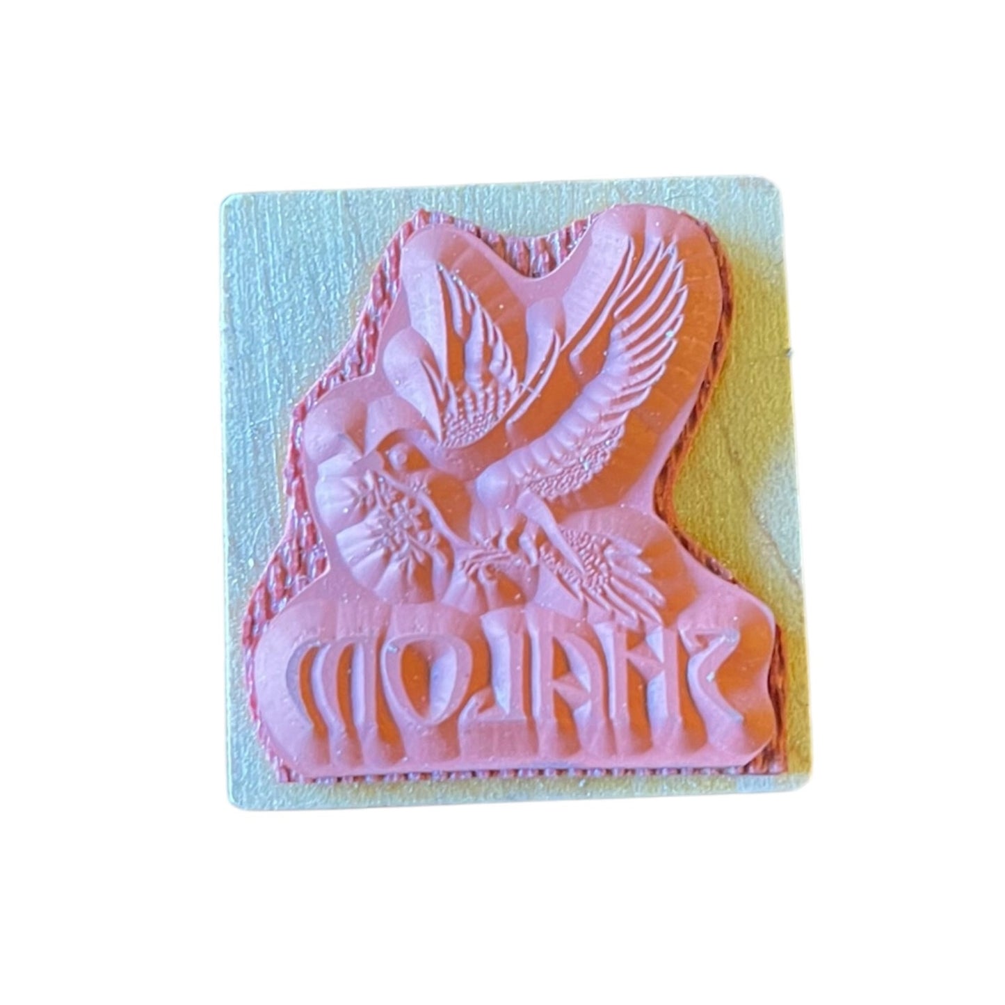 A pink rubber stamp featuring a bird design , shown on a wood block backing against a white background.