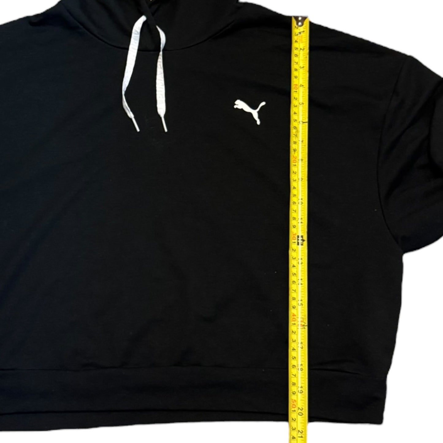 Black hoodie with a Puma logo being measured with a yellow tape measure.
