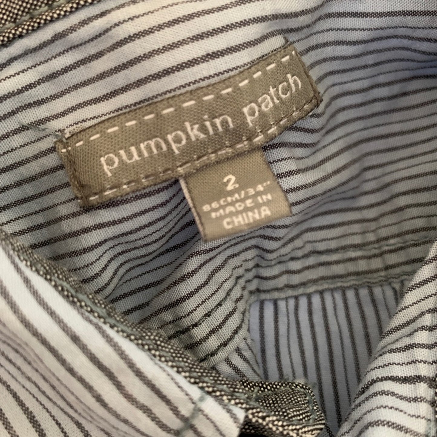 Close-up of a striped garment neck label reading 'pumpkin patch' with a size tag that says '2 86CM/34" MADE IN CHINA'.