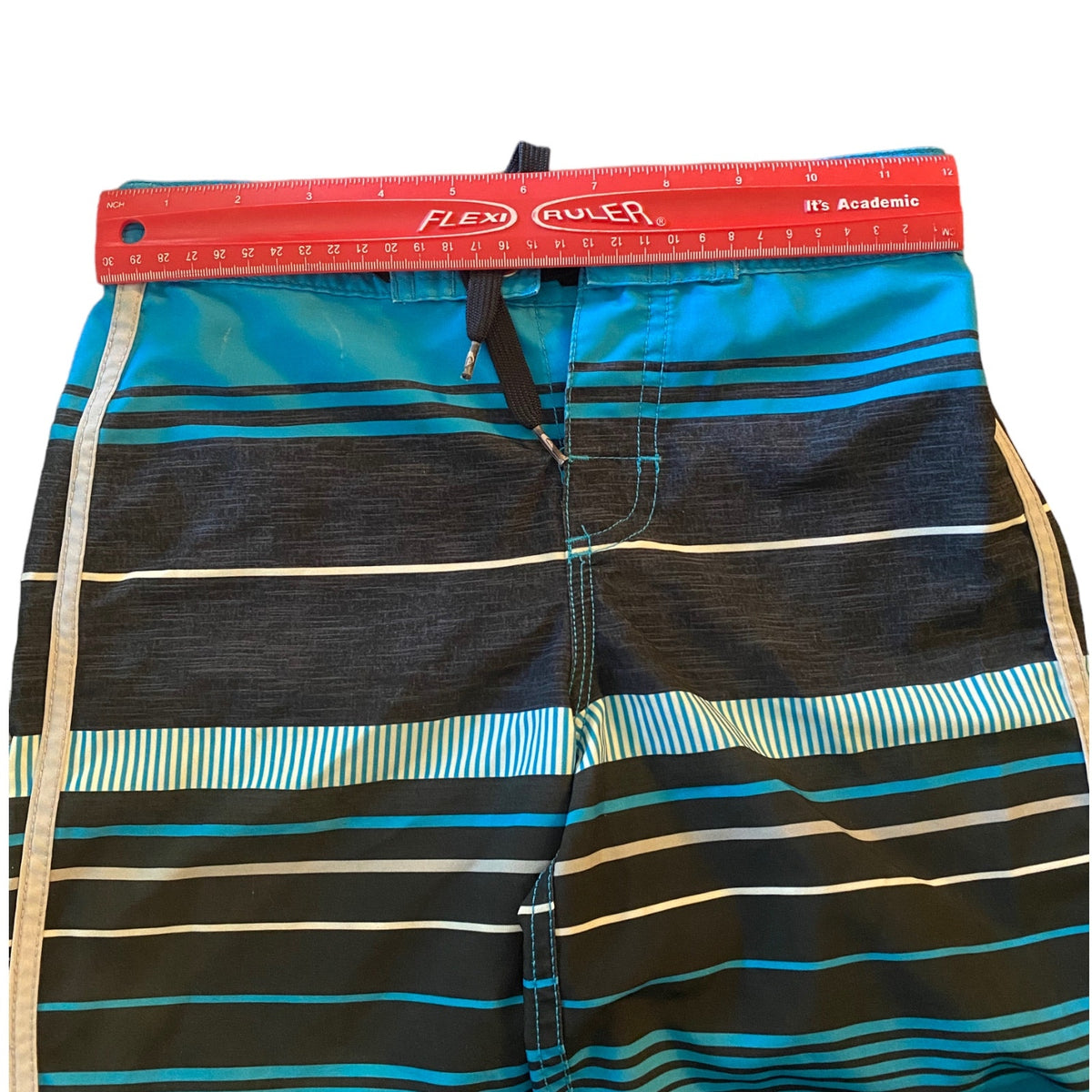 A pair of striped board shorts with a red ruler showing measurements.