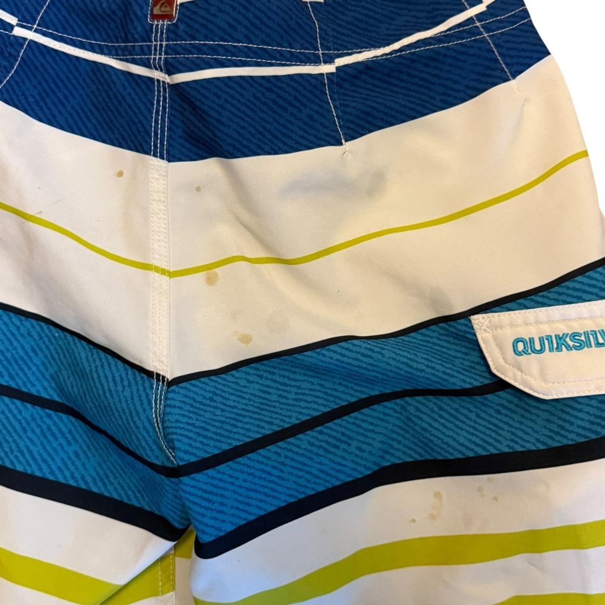 Close-up of Quiksilver board shorts stains and issues, stitching, and a side pocket with the Quiksilver logo.