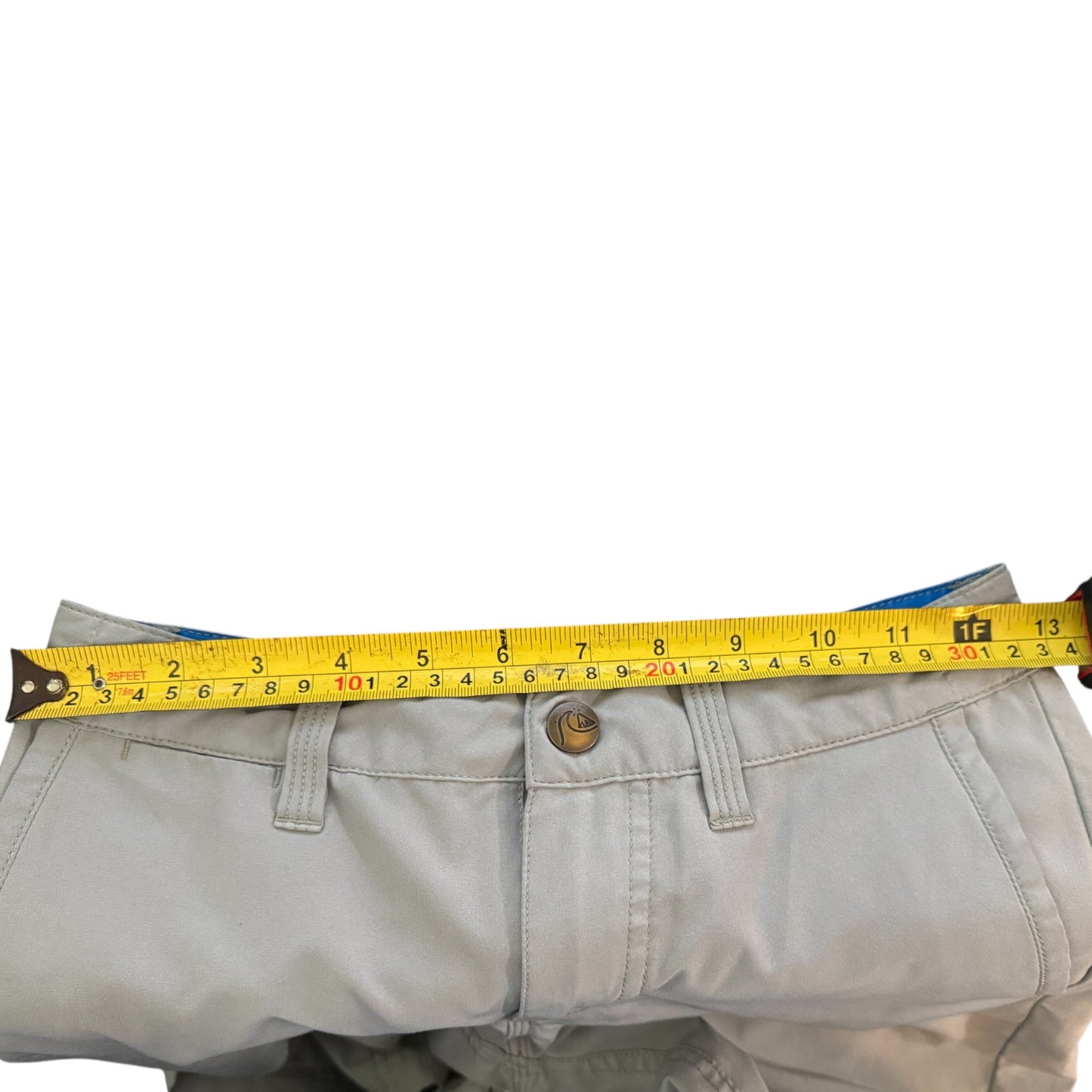 A yellow tape measure stretched horizontally across the waistband of light gray pants to show the measurement, photographed against a plain white background.