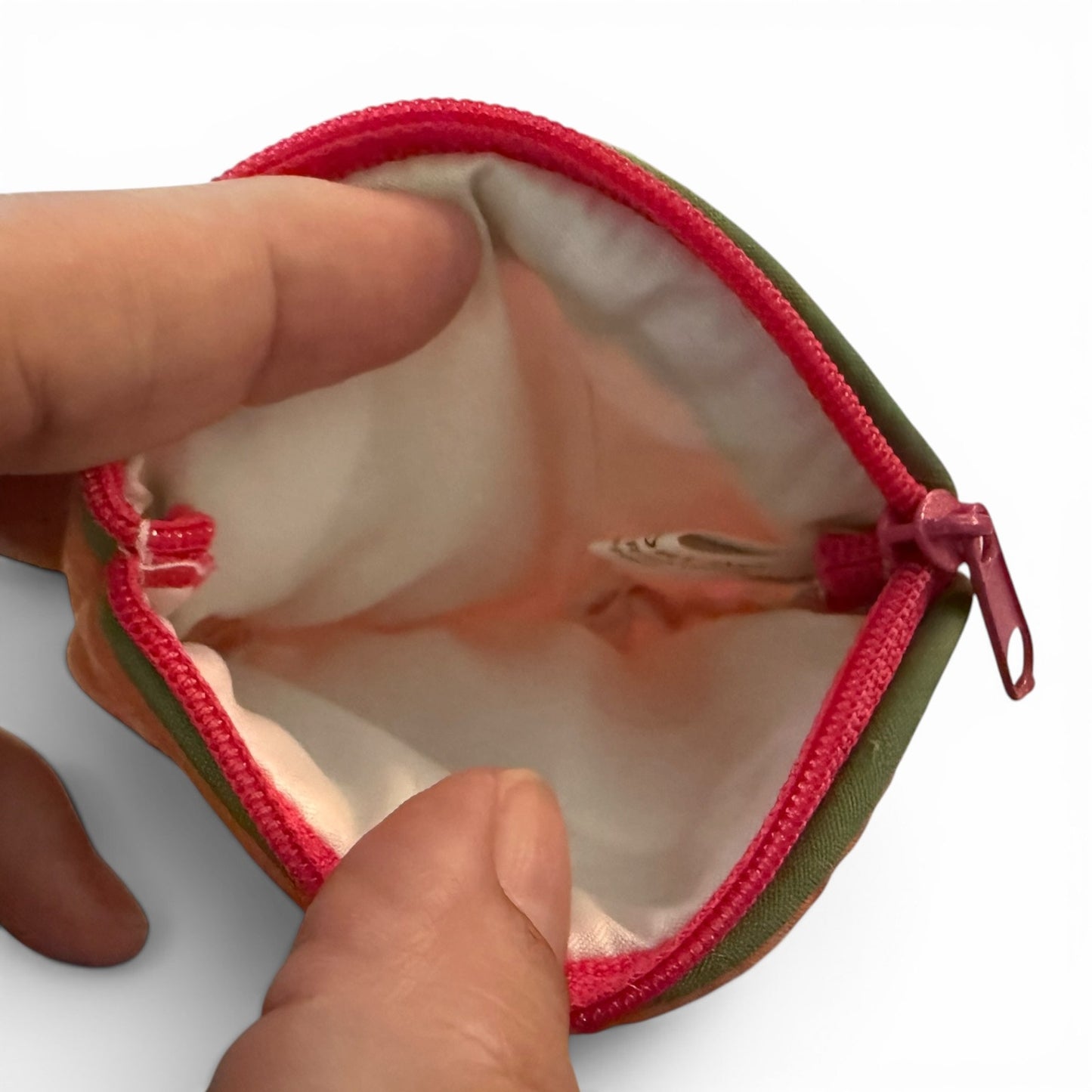 Small pouch with pink zipper being held open by a hand on a white background