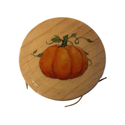 A round wooden lid featuring a painted orange pumpkin with green leaves and vines, shown on a plain white background.