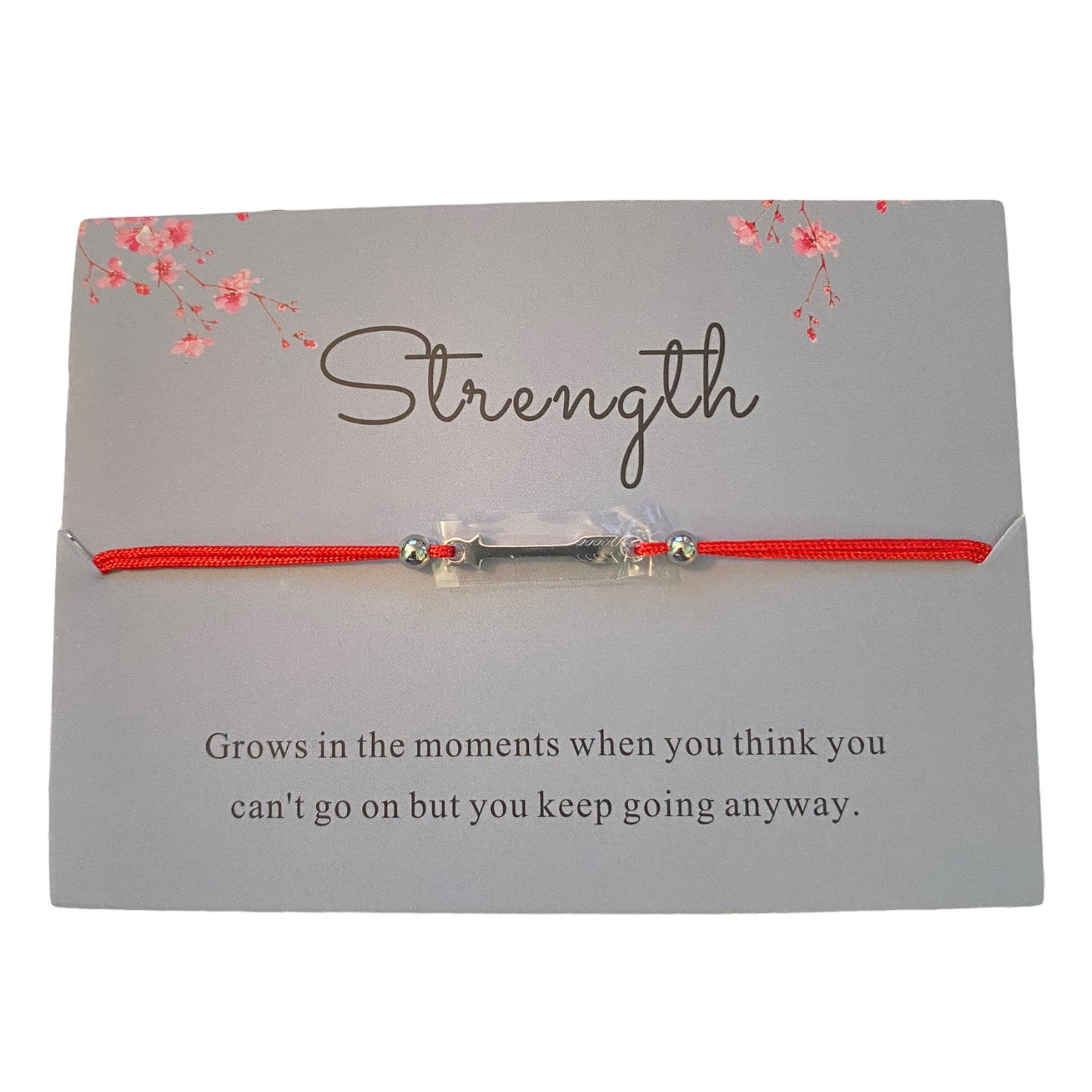 Red cord bracelet with silver charms with strength written on the card on a white background.