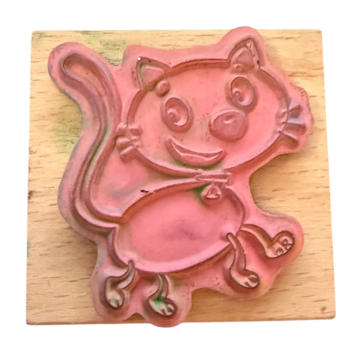 A pink cat-shaped rubber stamp with a smiling face, resting on a square light wood block.