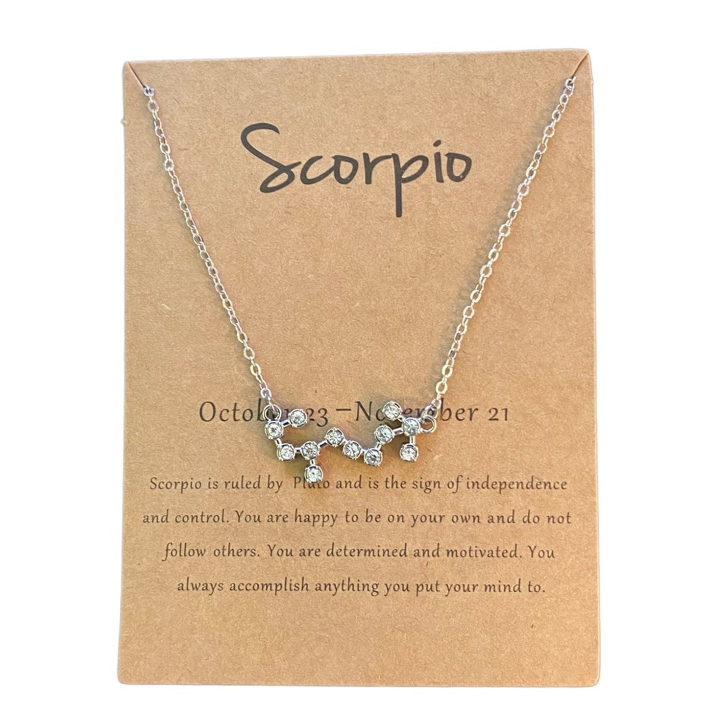 A silver chain necklace with a small cluster of clear rhinestones pendant, displayed on a brown kraft card labeled 'Scorpio' with astrological details.