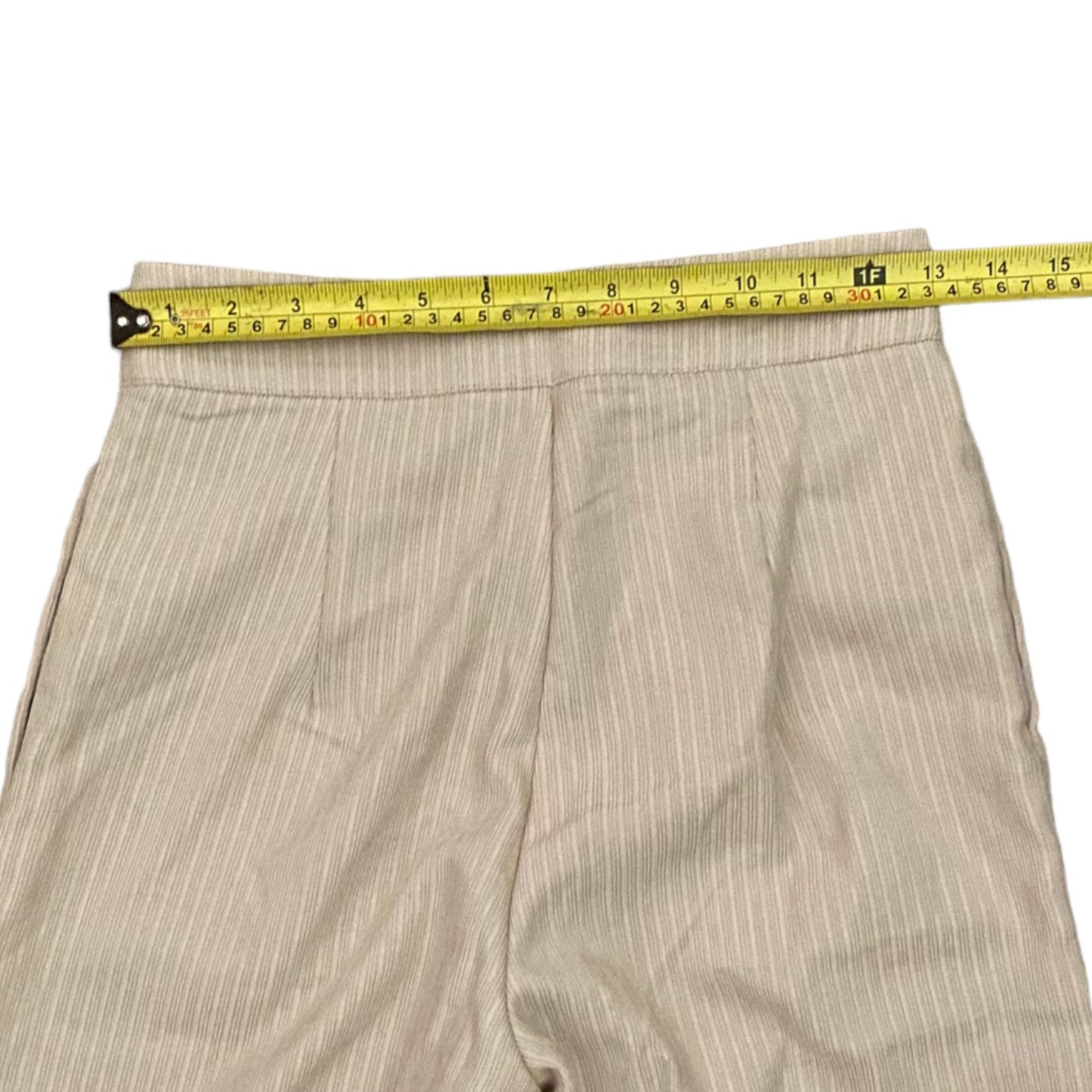 Beige pants laid flat on a white background, with a yellow tape measure stretched horizontally across the waistband to show the measurement.