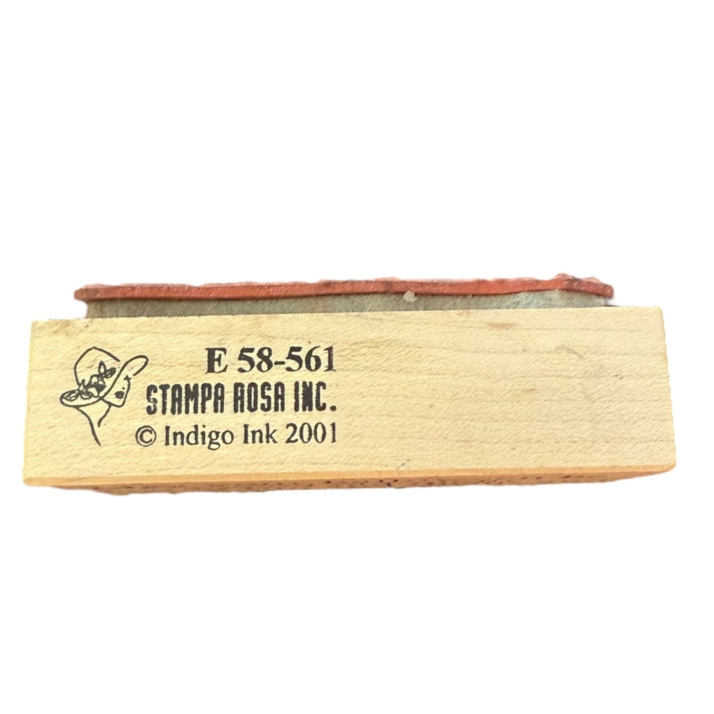 A wooden stamp block with a red rubber stamp head, featuring black printed text that reads 'E 58-561 STAMPA ROSA INC. © Indigo Ink 2001' on a plain white background.
