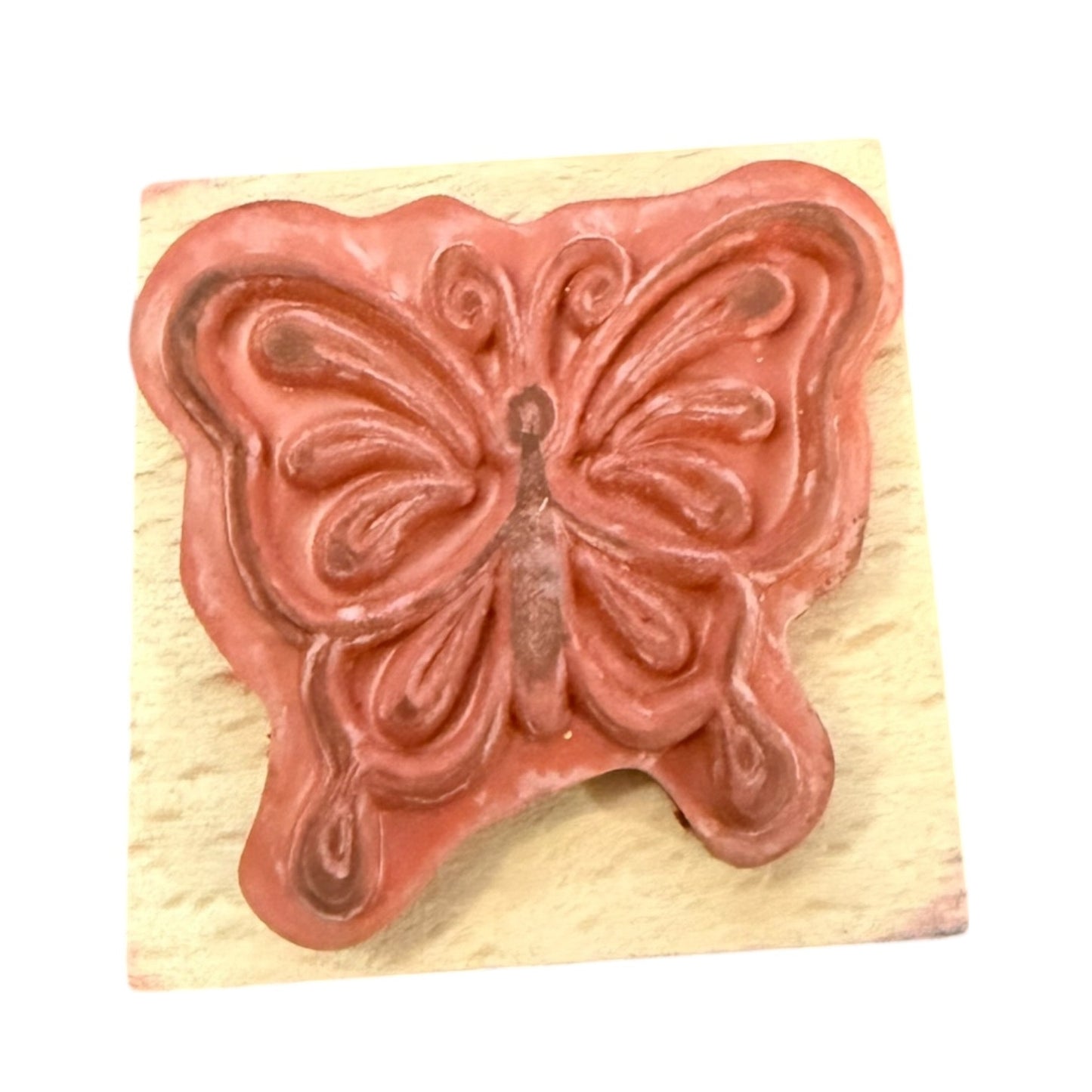 Butterfly-shaped stamp on a wooden block with a pinkish-brown design.