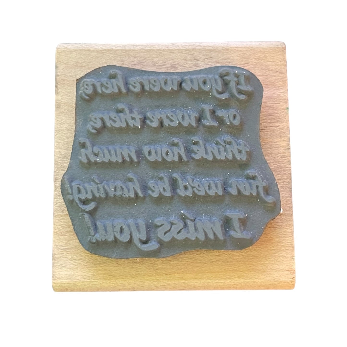 A dark gray rubber stamp with raised text, mounted on a square light wood block, shown against a plain white background.