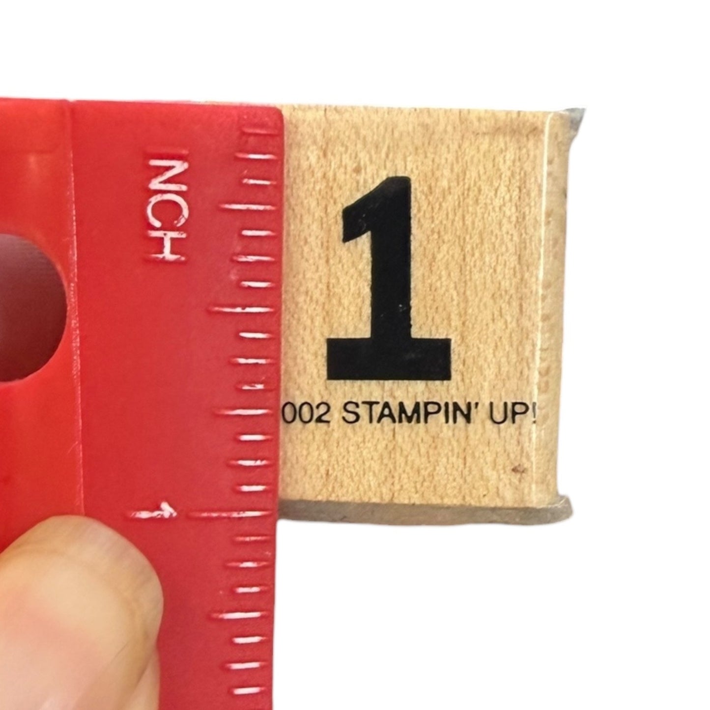Rubber stamp with number '1' and '002 Stampin' Up!' text, ruler reads 1" held by a hand against a white background.